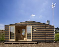 a small wooden cabin with a wind turbine in the background