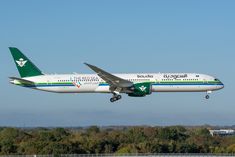 an airplane that is flying in the air with trees in the back ground behind it