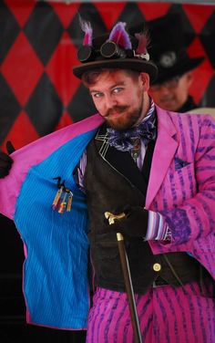 a man in a top hat and purple suit holding a pink coat over his shoulder