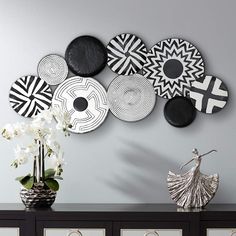 the wall is decorated with black and white plates on it, along with vases filled with flowers