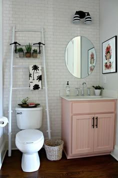 a white toilet sitting under a bathroom mirror next to a sink and a shelf filled with potted plants