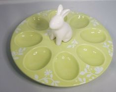 a small white rabbit figurine sitting on top of a green plate with holes in it