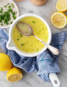 a white bowl filled with soup next to lemons and parsley on a marble surface