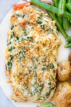 a white plate topped with meat covered in cheese next to green beans and broccoli