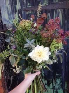 a person holding a bouquet of flowers in front of an old wooden door with peeling paint