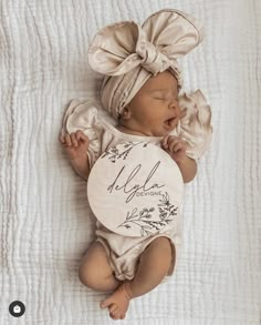 a newborn baby is wearing a headband and laying on a white blanket with her name written on it