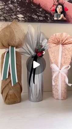 three wrapped presents sitting on top of a white table next to a painting and vase