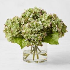 a glass vase filled with green flowers on top of a table