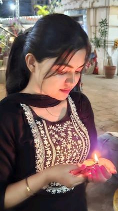 a woman is holding a lit candle in her hand and looking down at the ground