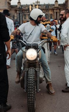 a man sitting on the back of a motorcycle in front of other men wearing white