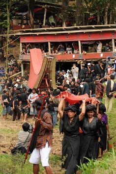 many people are carrying large objects on their heads as they walk up a hill in front of a crowd