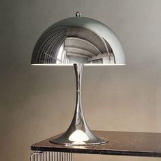 a table lamp sitting on top of a wooden table next to a metal rack and wall