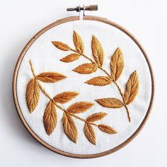 a close up of a embroidery on a white surface with a wooden hoop holding an embroidered leaf pattern