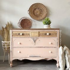 a pink dresser with two baskets on top of it and a plant in the corner