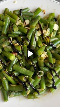 a white plate topped with green beans covered in black sauce and sprinkles