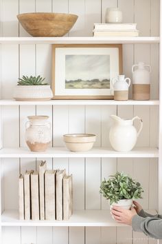 a white book shelf with books and vases on it