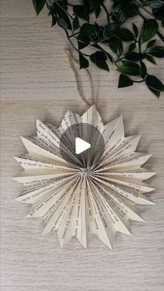 an ornament made out of book pages hanging on a wall next to a plant