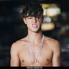 a shirtless young man with three necklaces on his chest and one earring