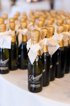 several bottles of champagne are lined up on a table with white and gold ribbon tied around them