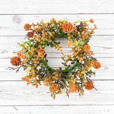 an orange and green wreath on a white wooden wall, with flowers in the middle