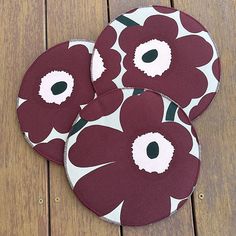 three red and white flowered coasters sitting on top of a wooden table