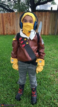 a little boy wearing a mask and holding a pair of scissors in his hands while standing on the grass