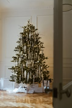 a small christmas tree in the corner of a room with boxes on the floor and presents under it