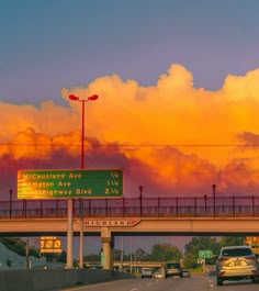 cars are driving on the highway under a cloudy sky with orange and pink clouds in the background