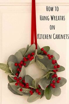 a wreath hanging on the wall with red ribbon and holly berry berries in front of it