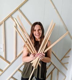 a woman standing in front of a white wall holding wooden sticks