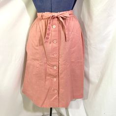 Vintage 80's pink midi skirt. The skirt is unbranded. It sits at the natural waist and has a gentle a line fit. The skirt buttons all they way down the front. It has two large side pockets. The skirt has a matching fabric belt. There is no fabric content tag but it feels like a lightweight polyester.  In very good vintage condition.  There are no size tags.  Measurements  Waist - 27 inches  Hip- 42 inches  Length- 25.5 inches High Waist Pink Skirt For Work, Pink High Waist Skirt For Work, Retro High Waist Relaxed Skirt, Pink High Waist Skirt For Workwear, Pink Full Skirt For Work, Retro Skirt For Spring Workwear, Long Pink Pencil Skirt For Spring, Pink Full Skirt For Workwear, High Waist Pink Pencil Skirt For Spring