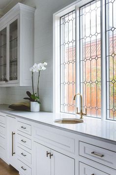 a kitchen with white cabinetry and glass front windows, along with a gold faucet