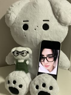 a white stuffed animal sitting next to a cell phone with glasses on it's face