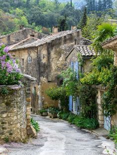 an alley way with stone buildings and flowers growing on the side of each building, surrounded by greenery