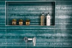 a green tiled bathroom with two shelves on the wall