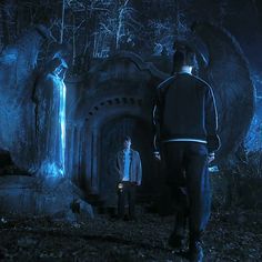 two men standing in front of a stone structure at night with blue light coming from it