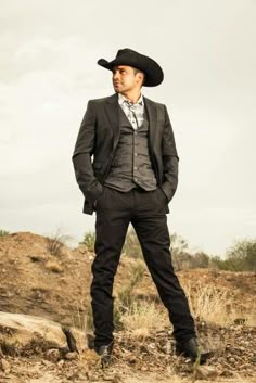 a man in a suit and hat standing on the ground with his hands behind his back