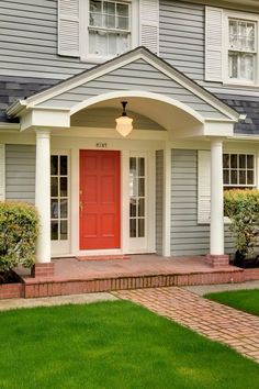 a red door is on the front of a gray house with white trim and brick steps