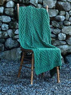 a chair with a blanket on it sitting in front of a stone wall and rocks