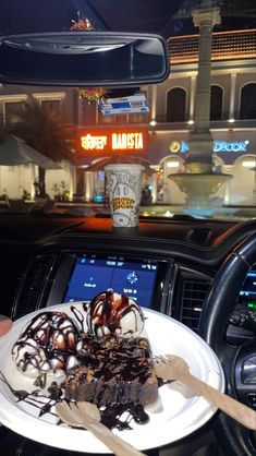 a person holding a plate with dessert on it in front of a car at night