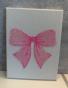 a pink bow is on the side of a white canvas with silver foil glitters