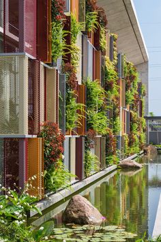 a building with plants growing on the side of it and water in front of it