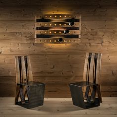 two wooden chairs sitting next to each other in front of a wall with wine bottles on it