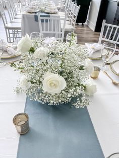 white flowers are in a vase on a blue table cloth at a formal dinner event