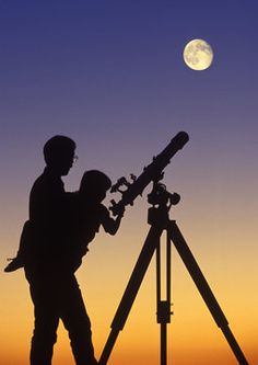 two people are looking at the moon through a telescope while it is set up to look into the sky