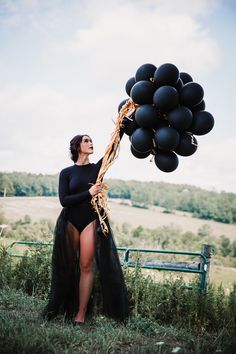 a woman in a black bodysuit is holding some balloons and posing for the camera