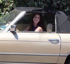 a woman sitting in the driver's seat of a tan car with an open top