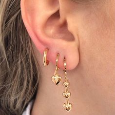 a close up of a person's ear wearing gold earrings with hearts on them