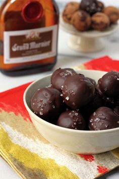 a bowl filled with chocolate covered donuts next to a bottle of wine and napkin