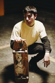 a young man squatting down with his skateboard in front of him on the ground